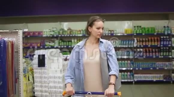 超市里穿着便服的女人推着购物车在找货物家庭主妇购物视频的预览图