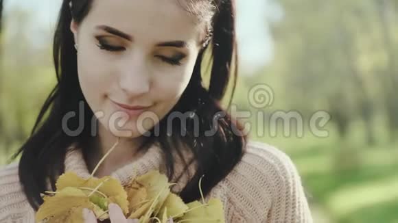 年轻漂亮女人的肖像布鲁内特穿毛衣的女孩和她手中的秋叶慢动作视频的预览图