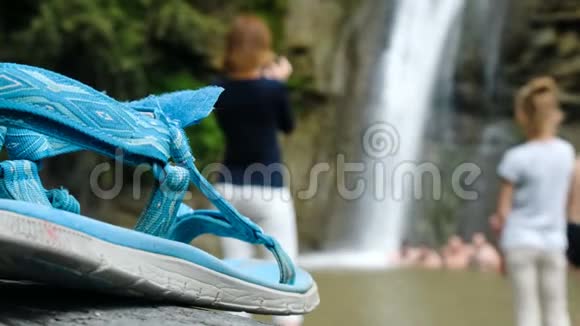 在人们在瀑布下散焦洗澡的背景下凉鞋的特写视频的预览图