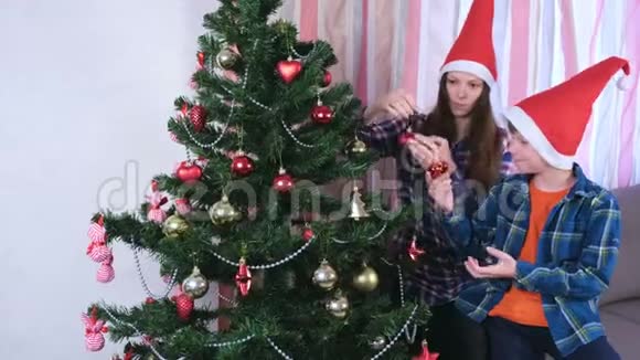 妈妈和儿子戴着圣诞帽用珠子和球装饰圣诞树家准备平安夜视频的预览图