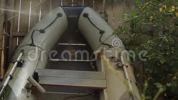 一个留胡子的人在他花园里的一个木栅栏的背景上洗了一艘装有高压水槽的PVC船视频的预览图