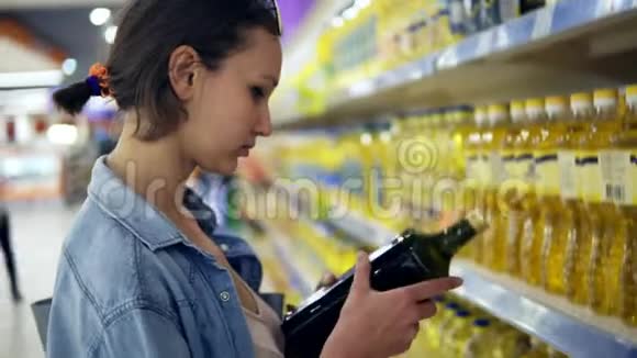 在超市里挑选产品的女人瓶油上的阅读标签把一个放进推车里任命视频的预览图
