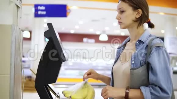 一个女孩在超市的电子秤上称重香蕉并贴上一张标价的贴纸玻璃纸中的香蕉视频的预览图