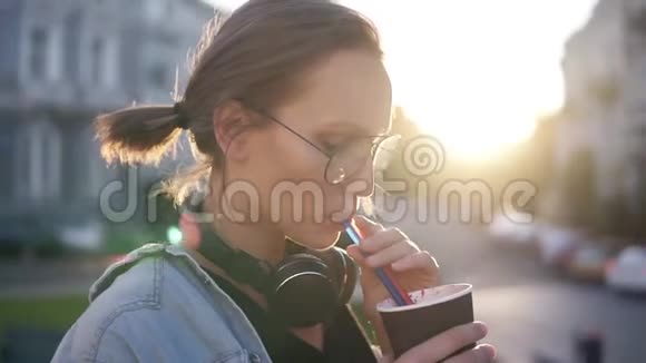 侧面看一个漂亮的年轻女人她的脖子上戴着耳机用吸管喝饮料金发女郎视频的预览图