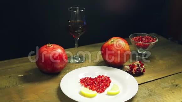 石榴籽的心脏放在一个用柠檬片装饰的白色盘子上桌子上有新鲜的石榴和一个视频的预览图