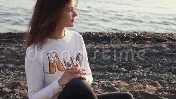 一个漂亮漂亮的女人坐在岩石海滩上视频的预览图