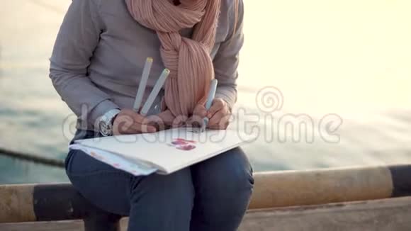 一位年轻的艺术家在等待她的朋友和大海时从事绘画工作视频的预览图