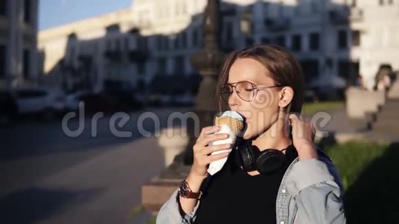 年轻女性穿着橙色衬衫在户外慢动作享受华夫饼锥中的软香草冰淇淋吃冰的女人视频的预览图