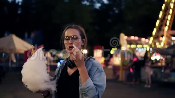在游乐园里一个戴着时髦眼镜的年轻女孩在吃糖果棉近距离拍摄摄像机显示器视频的预览图