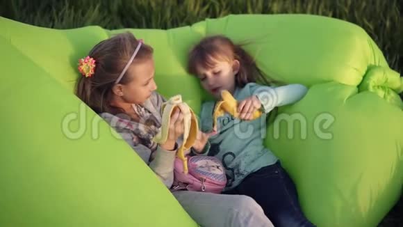 两个小妹妹躺在户外的充气绿色沙发上休息吃香蕉小个子舔手指成形术视频的预览图
