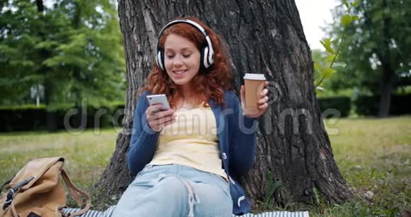 微笑的女孩用智能手机听音乐在公园放松视频的预览图