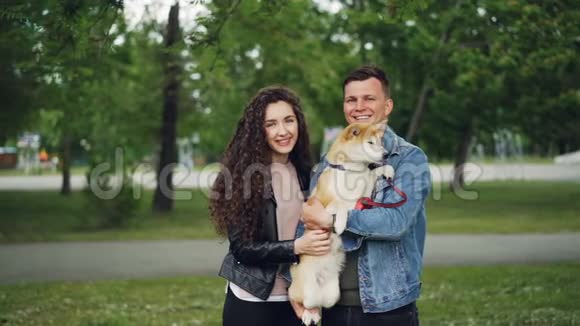 男人和女人的慢镜头肖像骄傲的狗主人抱着可爱的小狗看着相机微笑着站在里面视频的预览图