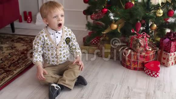 小孩坐在圣诞树旁打哈欠视频的预览图