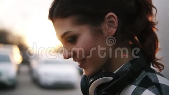 侧面看一个脖子上戴着耳机的女孩她微笑着转向模糊的视角长棕色视频的预览图