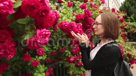 戴眼镜的年轻女人闻着花园里的玫瑰视频的预览图