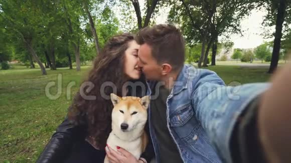 年轻的妻子和丈夫正在自拍与可爱的狗亲吻和拥抱对方和动物观点视频的预览图