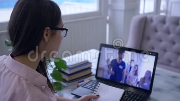 电子教育戴眼镜的女学生在笔记本上看视频时用钢笔在笔记本上写字视频的预览图