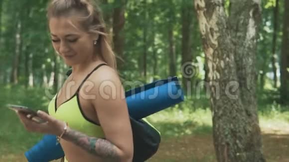 美丽的健身女人在公园里用手机走路可爱的女孩聊天视频的预览图