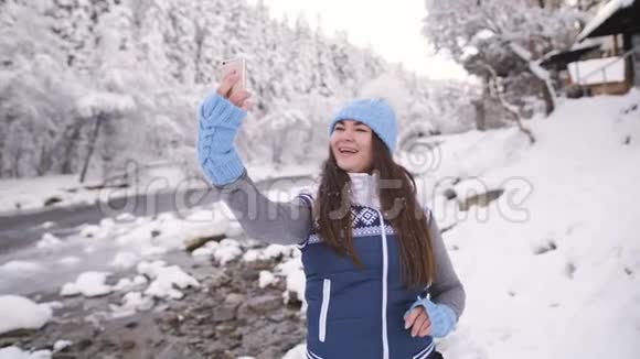 女孩在近山河的冬天森林里用手机视频交谈视频的预览图
