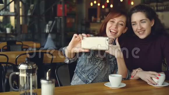 漂亮的女孩最好的朋友用智能手机自拍然后在咖啡馆喝咖啡时看照片视频的预览图