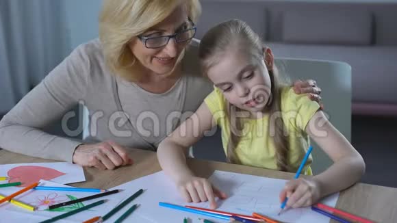 奶奶抚摸孙女的头可爱的女孩用彩色铅笔画房子视频的预览图