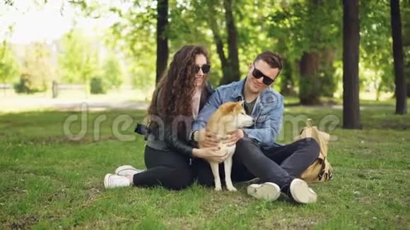 可爱的女孩和她的男朋友爱狗的主人周末在公园里拍宠物聊天休息视频的预览图