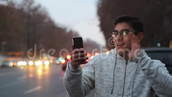 一个戴着眼镜穿着白色衬衫的家伙在Skype上用黑色电话交谈在移动汽车的背景上大笑视频的预览图
