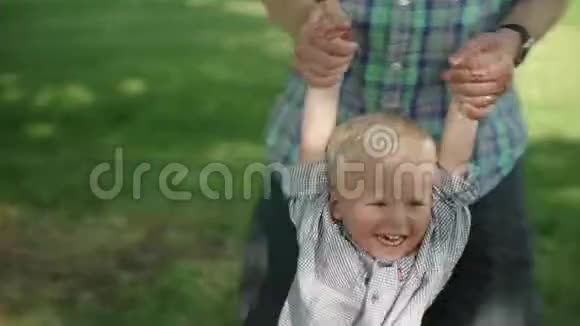 一个小男孩在公园里和他爸爸玩耍时的肖像爸爸摆动他的小男孩慢速高清视频的预览图