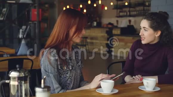 年轻女性在午餐时间在咖啡馆喝茶时使用智能手机聊天和做高五通信视频的预览图