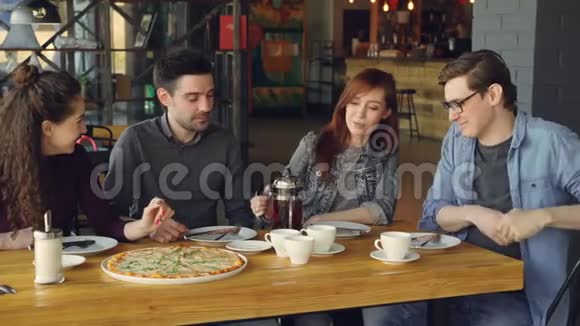 漂亮的年轻女人从茶壶里倒茶和坐在舒适的披萨咖啡馆里的朋友们聊天视频的预览图