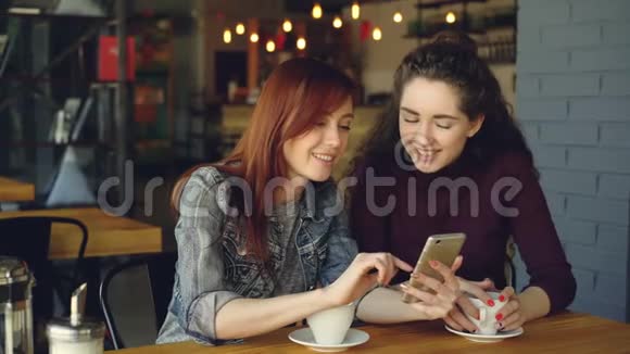 两个年轻漂亮的女朋友在咖啡馆里使用智能手机在感情上谈笑风生社交媒体会议视频的预览图