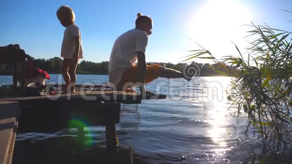 阳光明媚的夏日年轻人在湖边的木制码头上练习瑜伽小孩和他爸爸视频的预览图