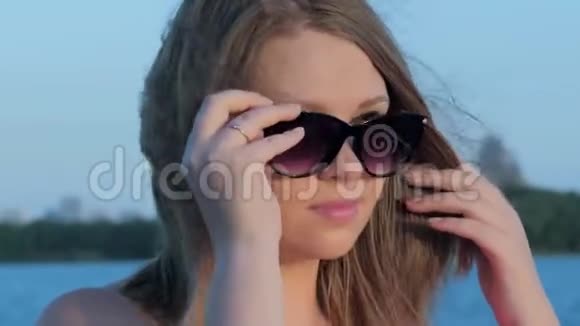 美丽微笑的白种人女孩在夕阳下戴上太阳镜模糊的背景视频的预览图