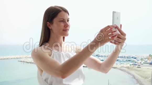 女人在阳台上使用手机女性在手机上慢动作欣赏海景并拍照视频的预览图