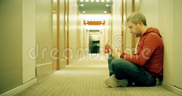 灰发男子穿着休闲装在酒店走廊里用智能手机视频的预览图