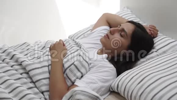 独自一人的黑发女人早上在卧室里醒来坐在床边视频的预览图