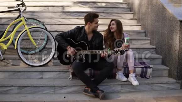 两个人坐在楼梯上弹吉他一个穿着黑色便装的男人和女友坐在一起玩吉他视频的预览图