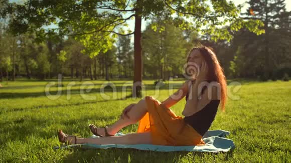 快乐的女性坐在草地上通过数字智能手机进行交谈视频的预览图
