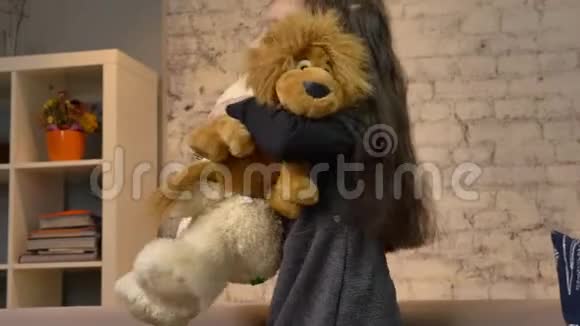 一个小女孩抱着一只玩具熊和一只玩具狮子坐在沙发上孩子们玩具回家视频的预览图