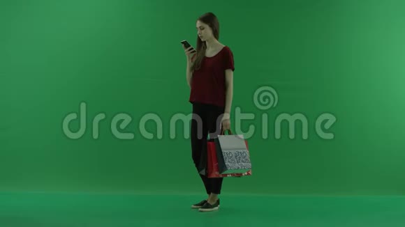 漂亮的购物女人用手机拿着购物袋女士正在上网或打字视频的预览图