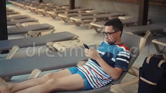 男人躺在躺椅上拿着智能手机视频的预览图