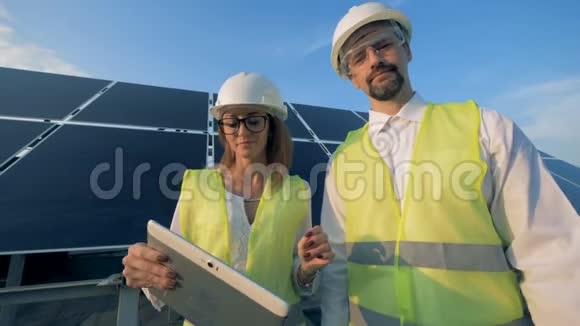两位兴高采烈的工程师正站在一个太阳能电池附近看着摄像机视频的预览图