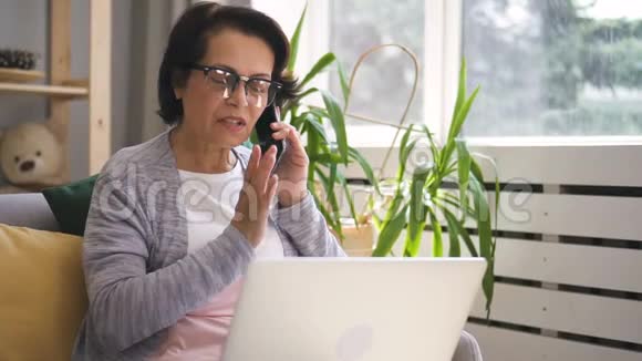 成熟的女商人正在打电话用笔记本电脑坐在家里视频的预览图