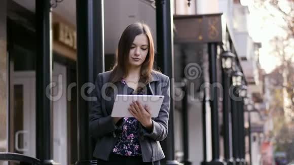 一幅美丽的年轻女商人的肖像她在夕阳下的商业附近的街道上使用平板设备视频的预览图