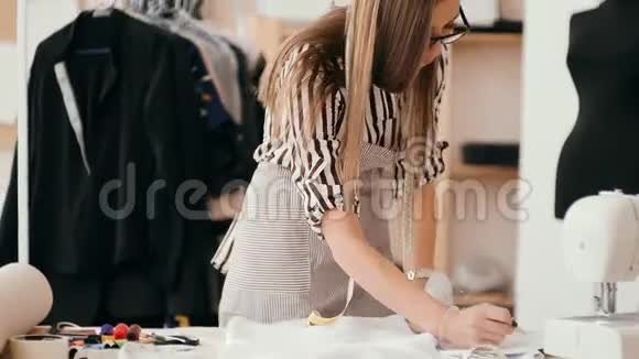 女裁缝在她阳光明媚的工作室里做缝纫机各种缝纫用品和布料摆在她周围视频的预览图