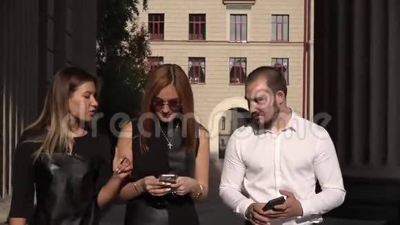 一名男学生和两名女学生在大学附近使用智能手机进行交流视频的预览图