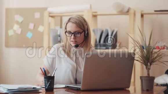 一个漂亮的年轻女孩在电话中心做接线员在耳机上讲话在电脑上工作视频的预览图