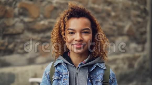 特写慢镜头肖像笑着的美国黑人女孩穿着牛仔夹克留着浅卷发看着相机和镜头视频的预览图