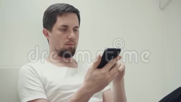 有胡子的年轻人正在玩智能手机坐在房间里视频的预览图