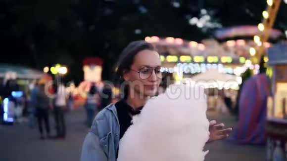 快乐年轻的女人在游乐园散步金发女人吃棉花糖享受她的时光微笑视频的预览图
